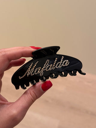 Hand holding a black hair clip with 'Mafalda' branding against a beige background